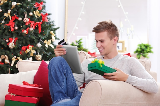 Giovane che fa shopping online con carta di credito a casa per Natale