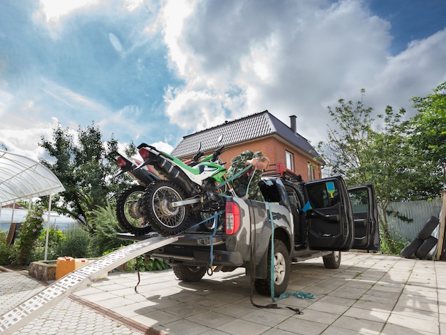 Giovane che fissa due dirt bike sportive al letto del camioncino usando la cintura di sicurezza blu.