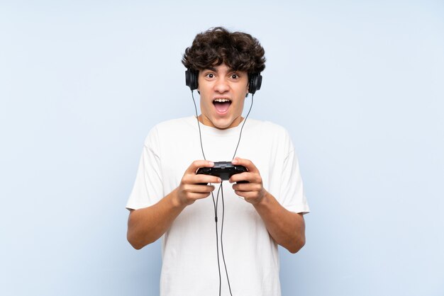 Giovane che gioca con un controller di videogioco sopra la parete blu isolata