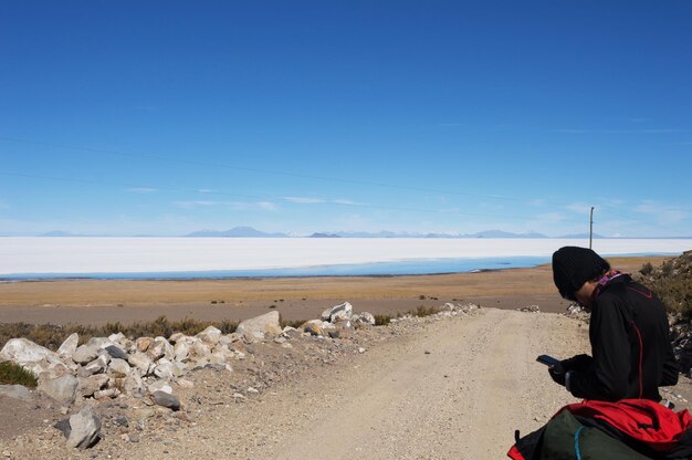 Giovane che guarda il cellulare mentre si appoggia ai bagagli di fronte al deserto salato