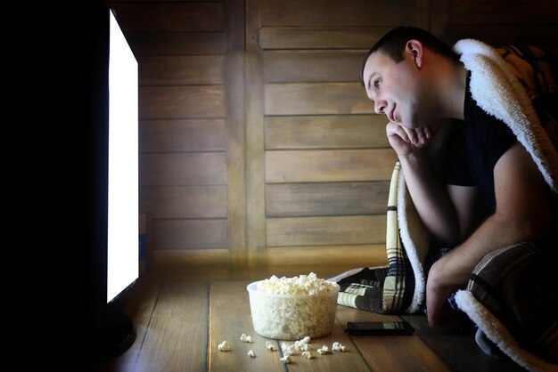 Giovane che guarda la televisione a casa sul pavimento e mangia popcorn