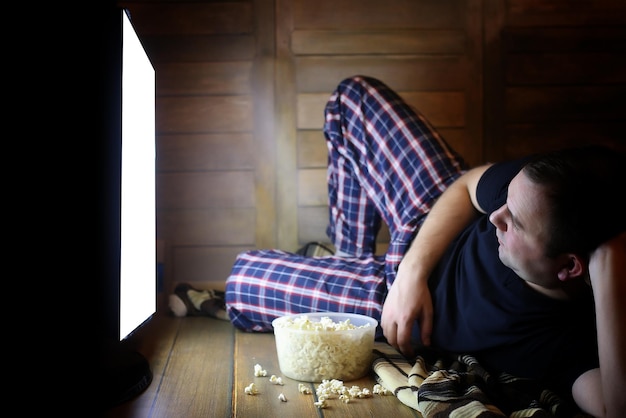 Giovane che guarda la televisione a casa sul pavimento e mangia popcorn