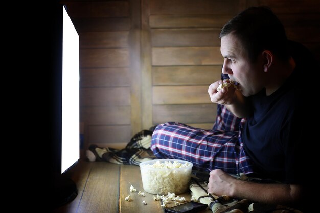 Giovane che guarda la televisione a casa sul pavimento e mangia popcorn