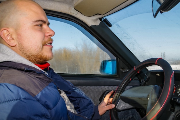 Giovane che guida un'auto sulla strada invernale. Vista interna