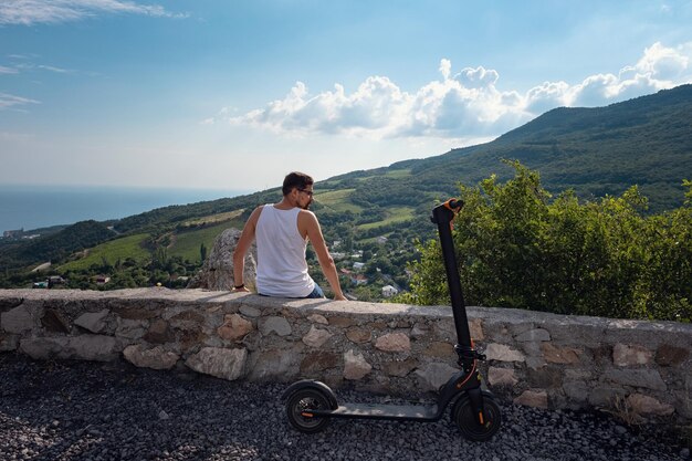 Giovane che guida uno scooter elettrico sulla catena montuosa Concetto di trasporto ecologico