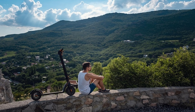 Giovane che guida uno scooter elettrico sulla catena montuosa Concetto di trasporto ecologico