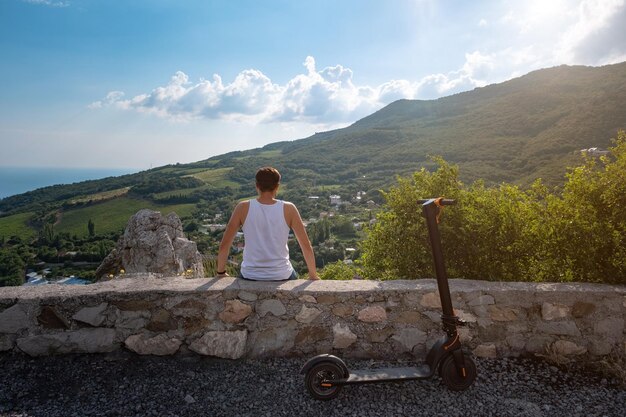 Giovane che guida uno scooter elettrico sulla catena montuosa Concetto di trasporto ecologico