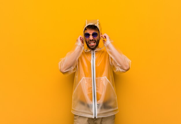 Giovane che indossa un cappotto di pioggia che copre le orecchie con le mani