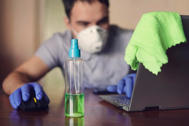 Giovane che indossa una maschera medica al lavoro dall'ufficio a casa a causa dell'epidemia di virus corona con laptop su un tavolo di legno lavoro a distanza sullo sfondo dell'ambiente domestico