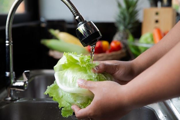 Giovane che lava una lattuga nel lavandino di cucina per produrre insalata