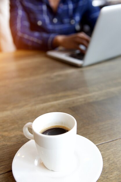 Giovane che lavora al computer portatile con la tazza di caffè al tavolo