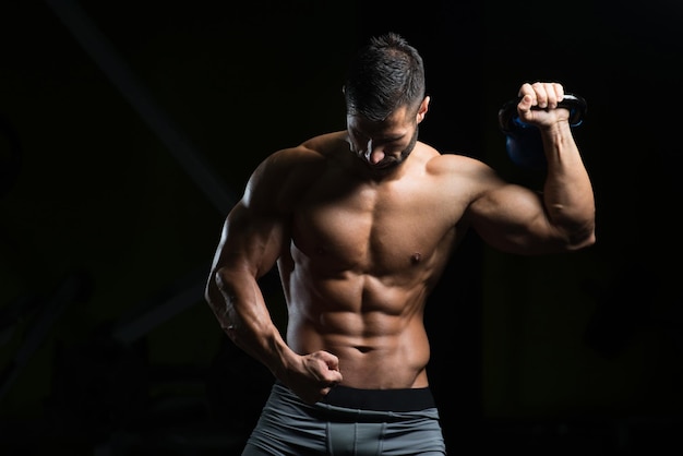 Giovane che lavora con il kettlebell in una palestra buia Bodybuilder facendo esercizi pesanti con Kettlebell