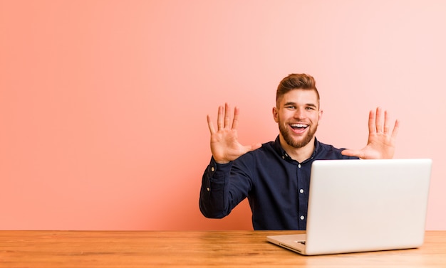 Giovane che lavora con il suo computer portatile che mostra numero dieci con le mani.