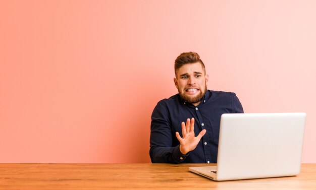 Giovane che lavora con il suo laptop rifiutando qualcuno che mostra un gesto di disgusto.