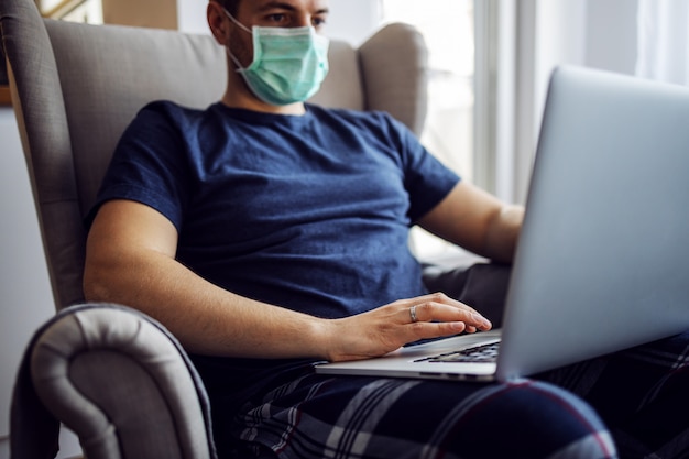 Giovane che lavora da casa, durante la quarantena. Indossare una maschera per misure protettive. Resta a casa.