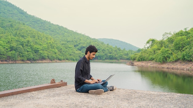 Giovane che lavora su un laptop e seduto nella natura Concetto di lavoro e nomade digitale