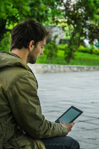 Giovane che legge con una tavoletta digitale al parco