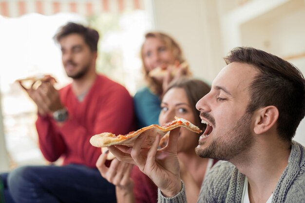 Giovane che mangia pizza a casa con gli amici
