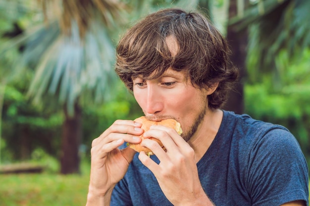 Giovane che mangia un hamburger nel parco.