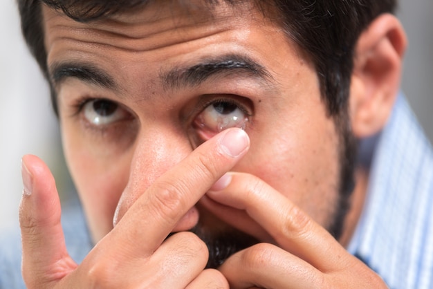 Giovane che mette lenti a contatto nel suo occhio sinistro, da vicino