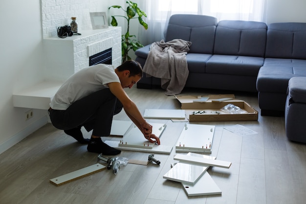 giovane che mette mobili da assemblare mentre si trasferiscono nella tua nuova casa.