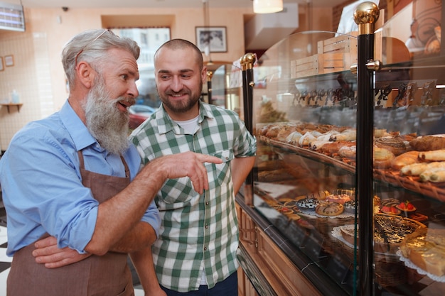 Giovane che parla con un fornaio anziano mentre fa acquisti per pasticceria al panificio locale