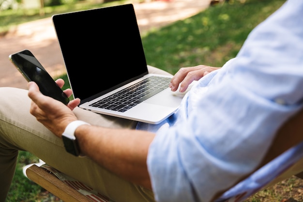 Giovane che per mezzo del computer portatile e del telefono cellulare.