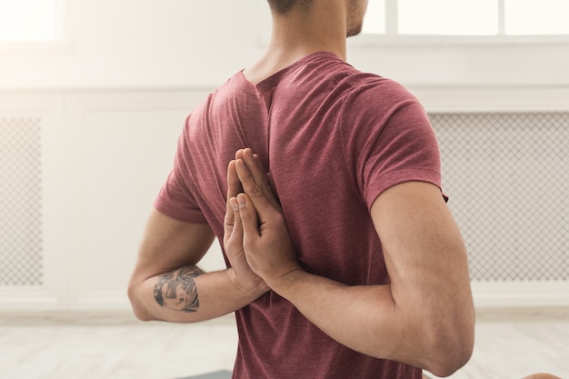 Giovane che pratica yoga, facendo esercizi di asana. Guy fa la posa di preghiera inversa, allungamento della schiena e delle spalle. Stile di vita sano, copia spazio