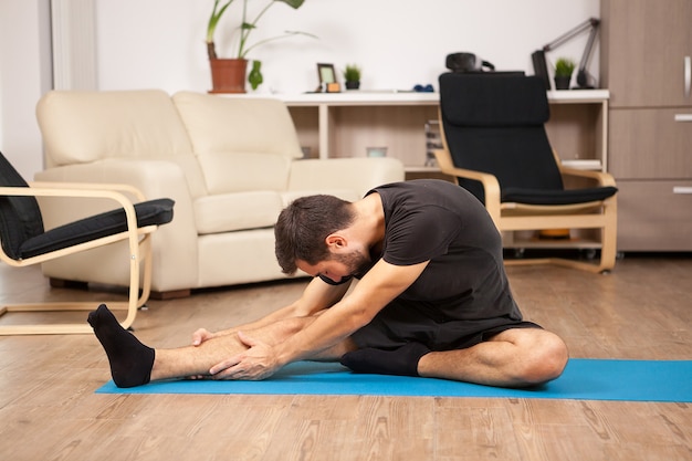 Giovane che pratica yoga nel suo salotto di casa. È stremato e si sente rilassato