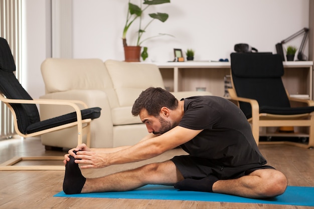 Giovane che pratica yoga nel suo salotto di casa. È stremato e si sente rilassato