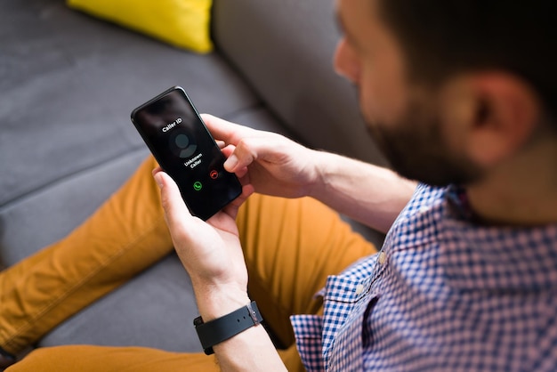 Giovane che riceve una telefonata sul suo smartphone mentre riposa sul divano di casa