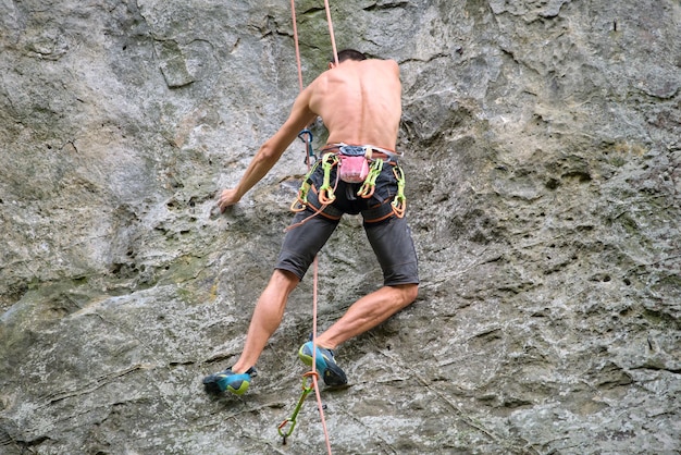 Giovane che scala la parete ripida della montagna rocciosa Lo scalatore maschio supera il percorso impegnativo. Impegnarsi nel concetto di sport estremo.