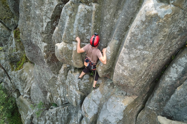 Giovane che scala parete ripida della montagna rocciosa. Lo scalatore maschio supera il percorso impegnativo. Impegnarsi nel concetto di sport estremo.