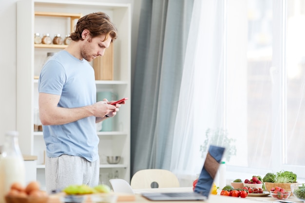 Giovane che scrive un messaggio sul telefono cellulare mentre si trovava in cucina al mattino