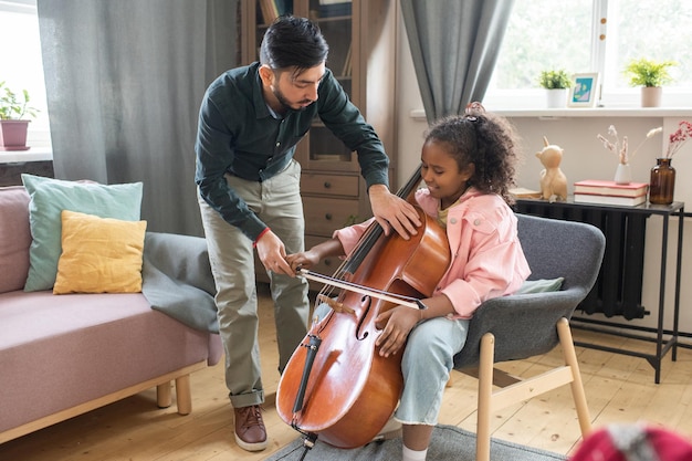 Giovane che si china su una scolaretta carina e diligente con il violoncello