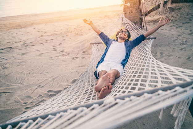 Giovane che si distende in hammock sulla spiaggia. Felicità, libertà di vacanza e concetto di viaggio. Braccia aperte