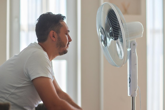 Giovane che si rilassa sotto il ventilatore dell'aria a casa