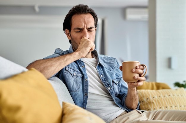 Giovane che si sente male e beve il tè mentre tossisce a casa