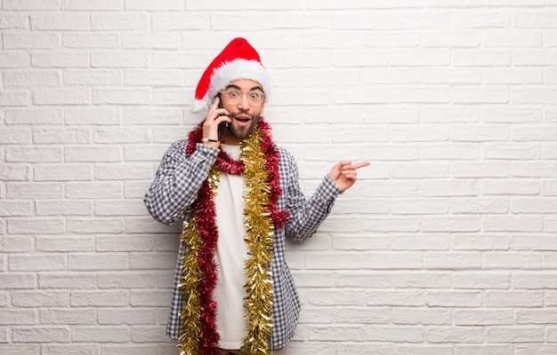 Giovane che si siede con i regali che celebrano natale che tiene qualcosa con la mano