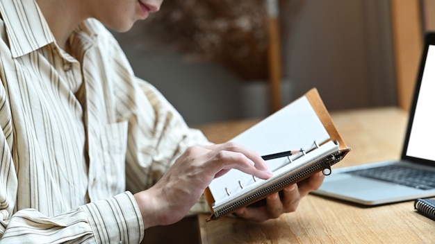 Giovane che si siede davanti al suo computer portatile e controlla le informazioni sul taccuino.