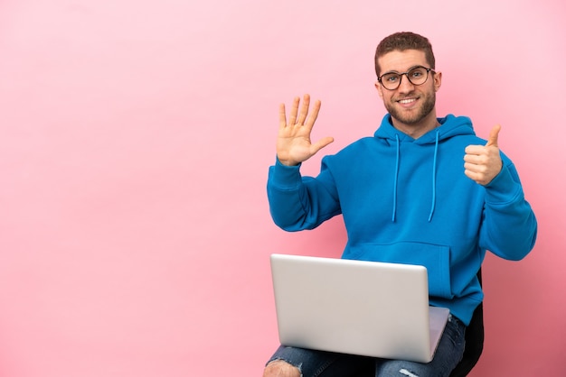 Giovane che si siede su una sedia con il computer portatile che conta sei con le dita