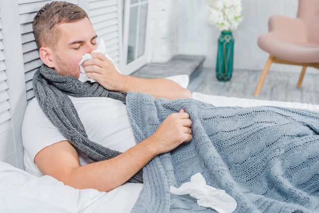 Giovane che si trova sul letto con tessuto con influenza o allergia