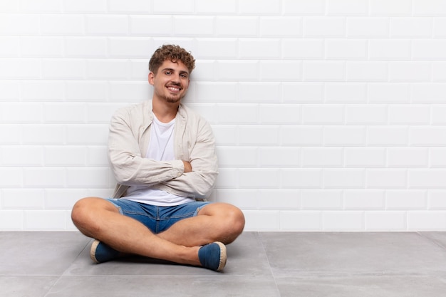 Giovane che sorride alla macchina fotografica con le braccia incrociate e un felice