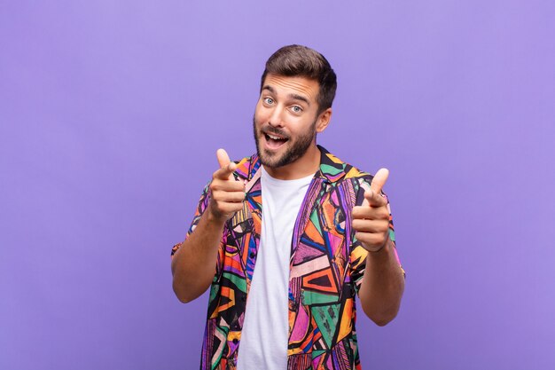 Giovane che sorride con un atteggiamento positivo, di successo, felice che indica la macchina fotografica, facendo il segno della pistola con le mani