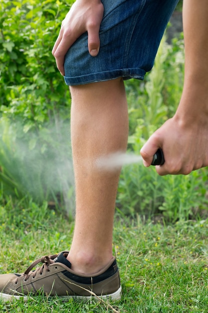 Giovane che spruzza repellente per insetti per zanzare nella foresta