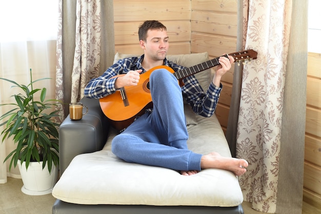 Giovane che suona la chitarra e si siede sul divano la mattina del fine settimana