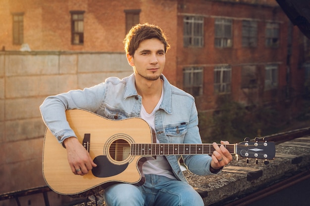 Giovane che suona la chitarra in città sullo sfondo dei raggi del sole