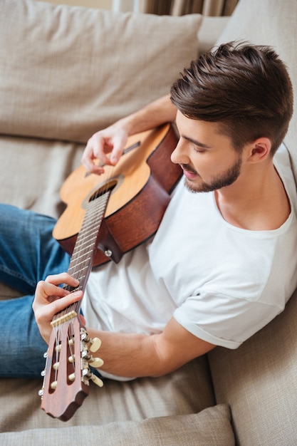 Giovane che suona la chitarra sul divano di casa