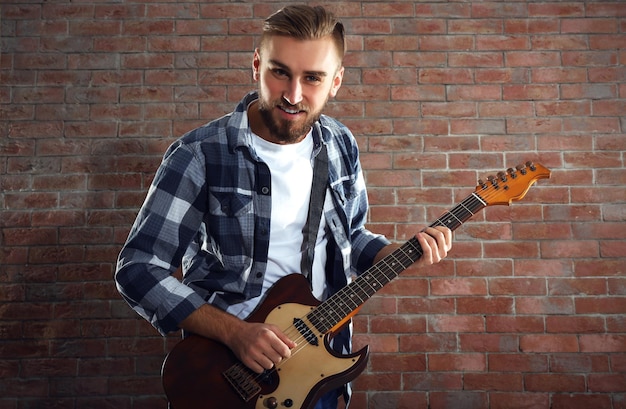 Giovane che suona la chitarra sul fondo del muro di mattoni