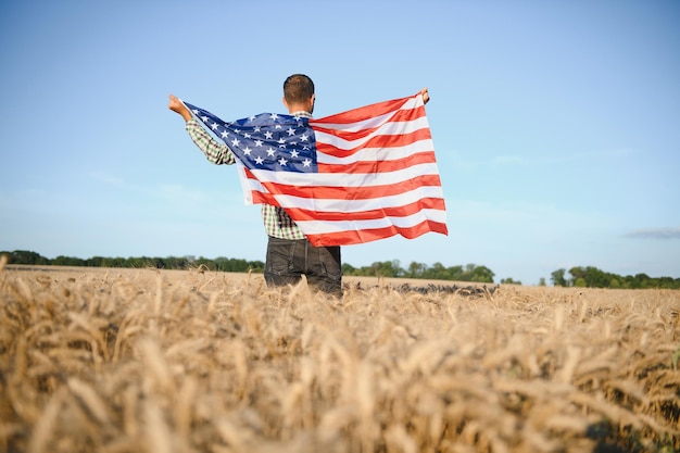 Giovane che tiene bandiera americana in piedi nel campo di grano